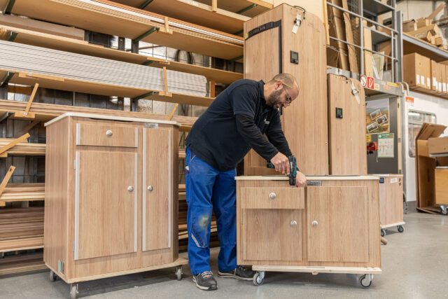 In der Fertigungshalle der Tischer Manufaktur schiebt ein Mitarbeiter ein fertig montiertes Küchenmodul durch die Werkstatt.