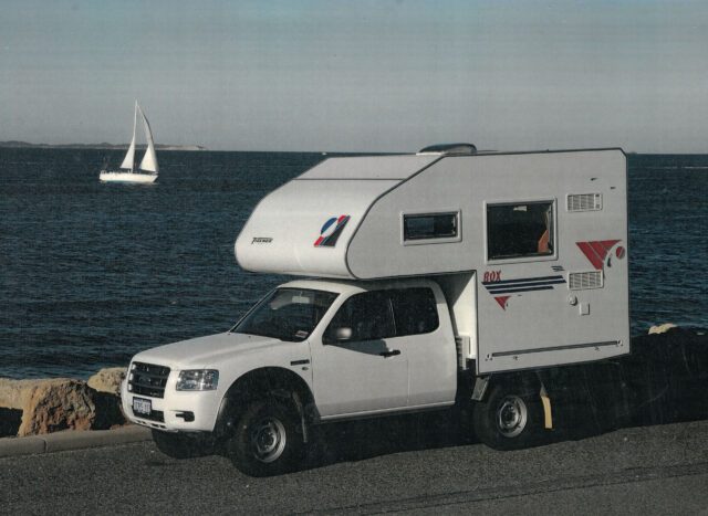 2001_Tischer-Kabine auf weißem Pick-up – Aufnahme vor dem Meer mit Segelboot.