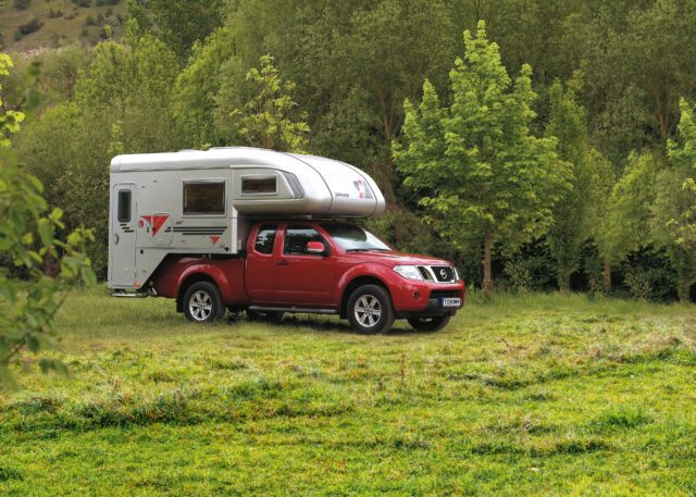 Tischer-Wohnkabine auf rotem Nissan Navara – seitlicher Blick, Camper steht auf Wiese.