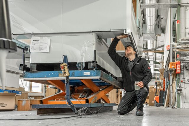 Mitarbeiter in der Tischer Werkstatt an Bearbeitungsstation – zeigt auf Bauteil der Kabine.