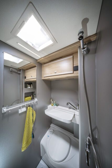 Tischer Wohnkabine mit Kompaktem Badezimmer mit Duschfunktion, Waschbecken und Toilette – helles Tageslicht durch Dachluke.