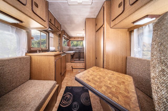 Retro-inspirierte Wohnkabine mit gemustertem Tisch und Holzdekor, Blick Richtung Küche.