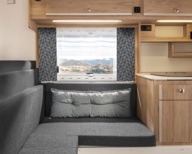 Tischer Wohnkabine mit grauen Polstern und Vorhängen mit dunkelgrauem Muster.