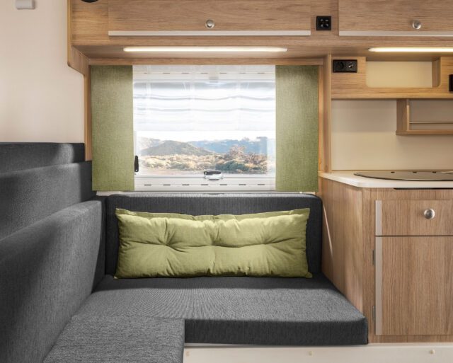 Wohnbereich in Tischer Kabine mit hellblauen Polstern und grünen Vorhängen.