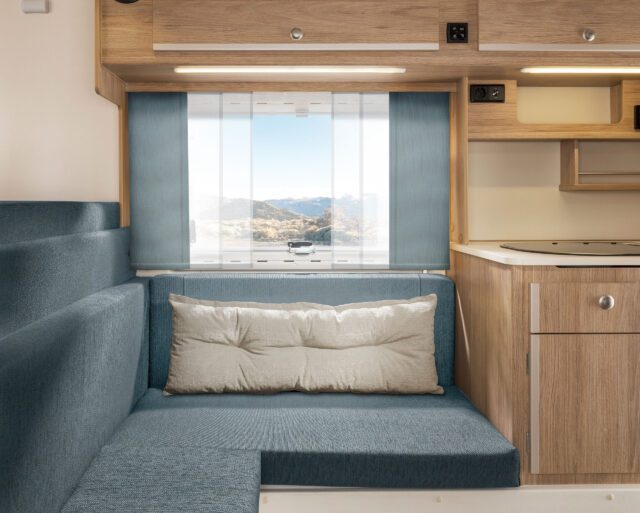 Sitzgruppe in Tischer Wohnkabine mit blauen Polstern und hellem Vorhangstoff.