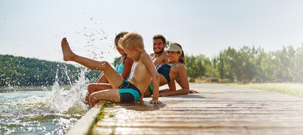 Familie am See badet glücklich mit Füßen im Wasser im Sommer