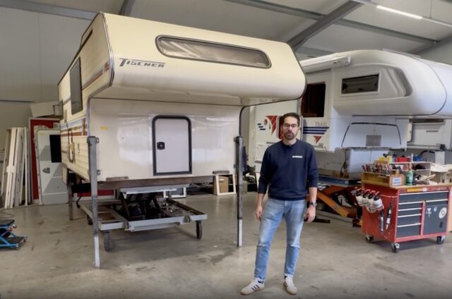 Alte Tischer Kabine auf Stützen in Produktionshalle, Mitarbeiter davor. Restaurierung