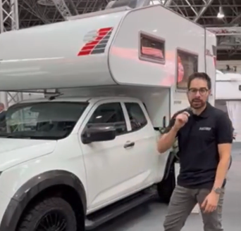 Tischer Wohnkabine auf weißem Nissan Navara Pickup, Mitarbeiter erklärt Funktionen am Messestand.